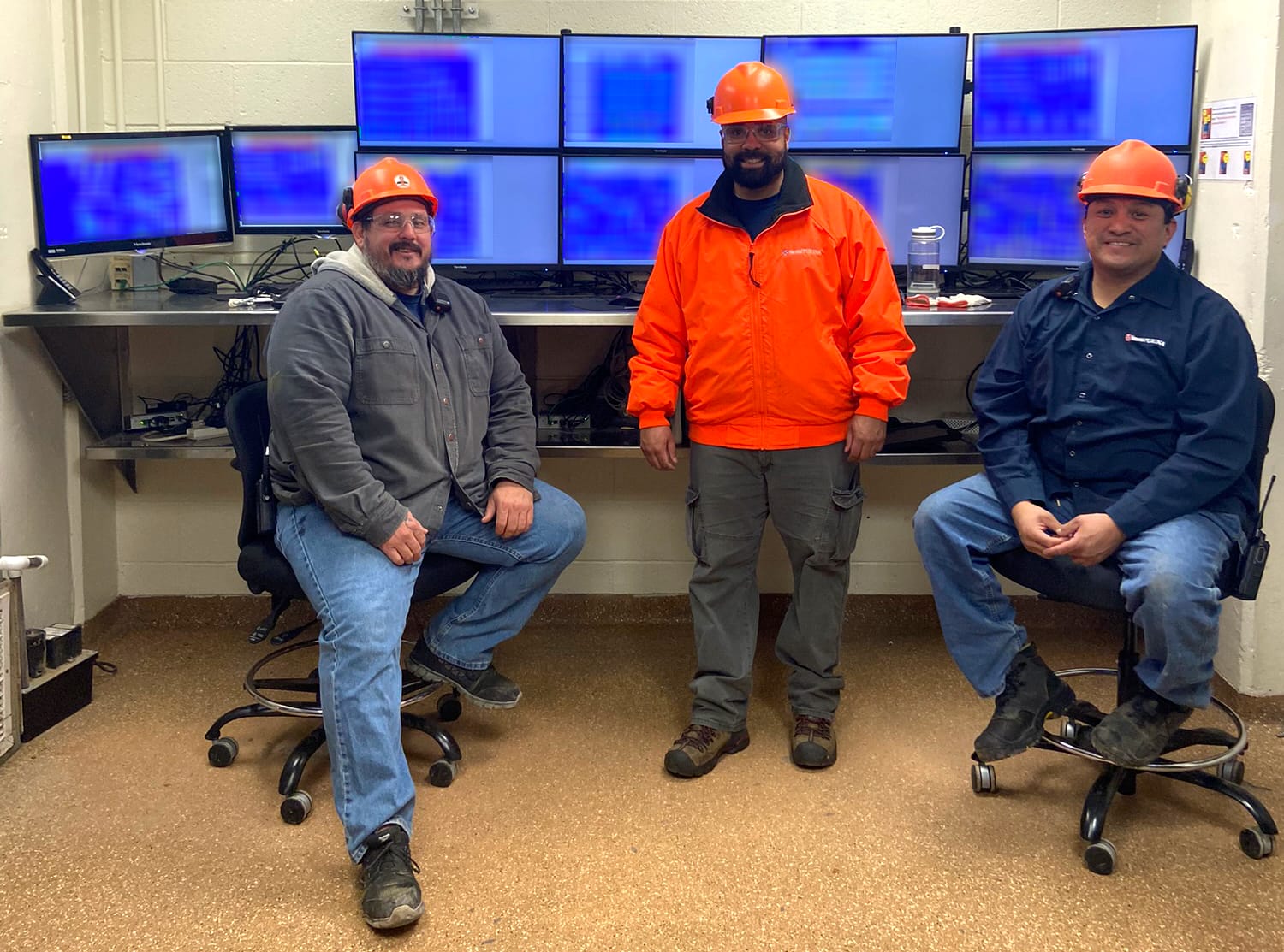 Three Purina employees, wearing hardhats, pose in front of the Flagstaff plant control computers. 